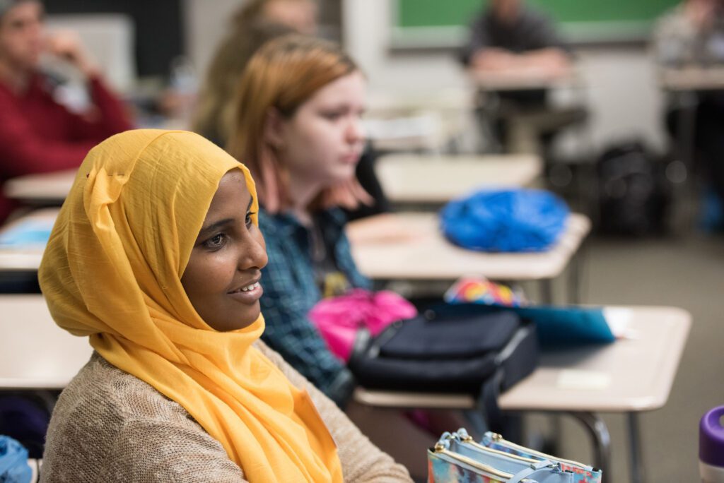 A female student in a hijab smiles as she listens to someone else speaking.