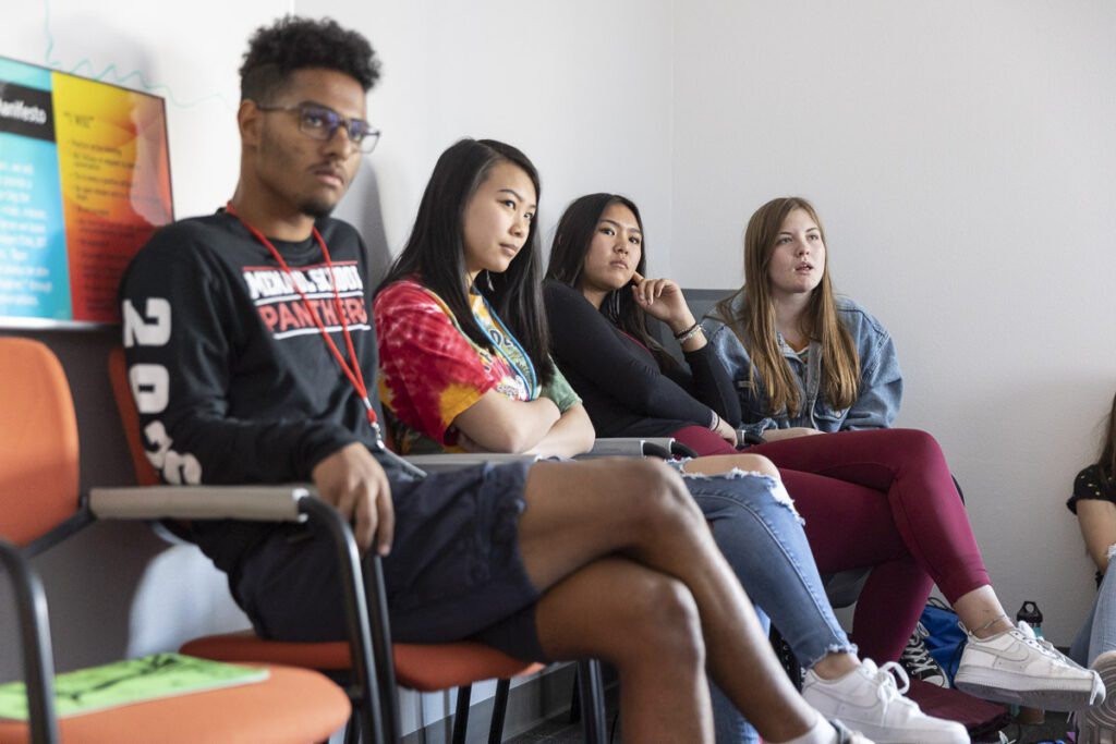 Four students sit in a chair listening to a speaker (off-picture).